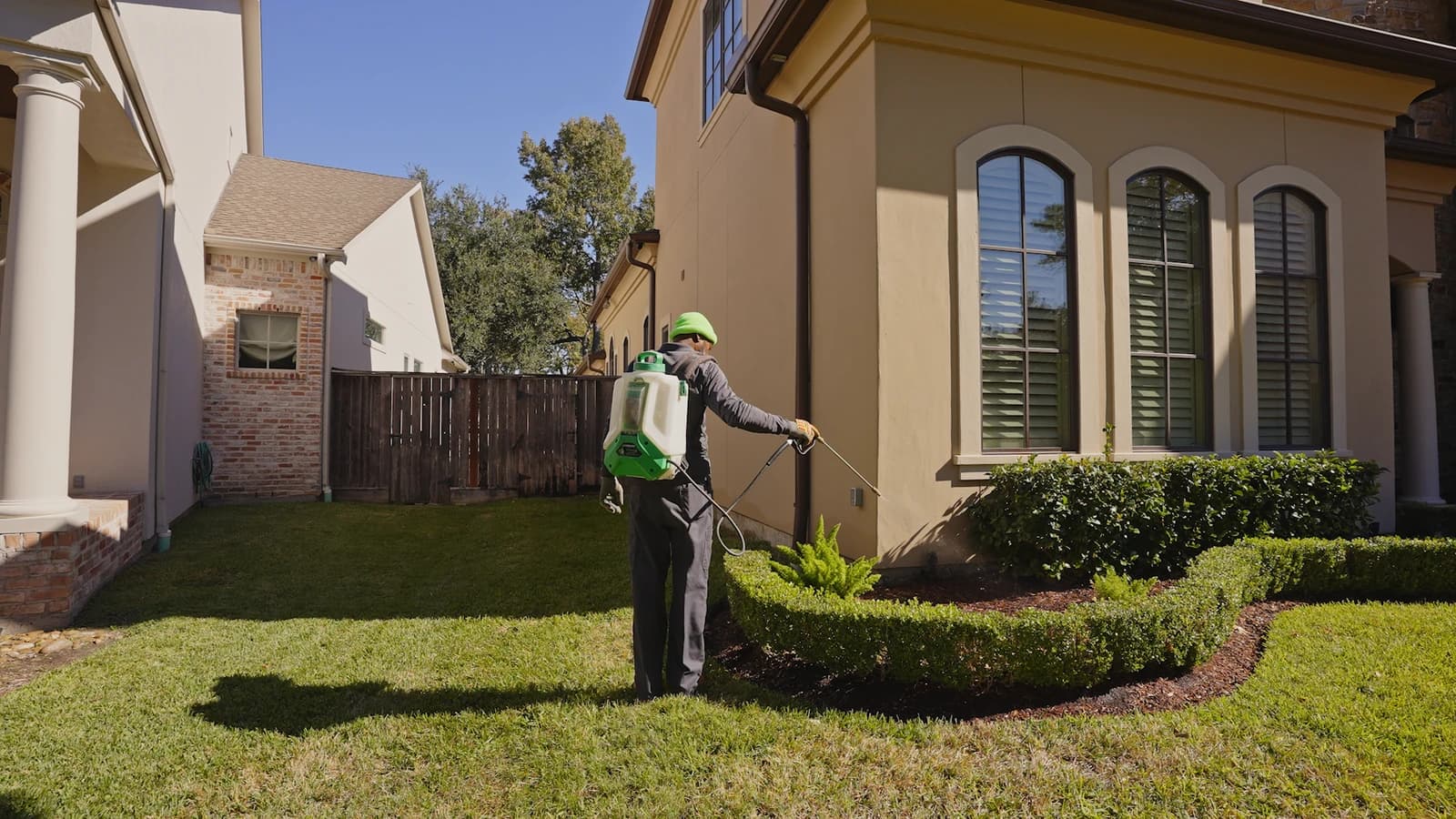 Technician applying a foundation spray along the exterior wall of a suburban home